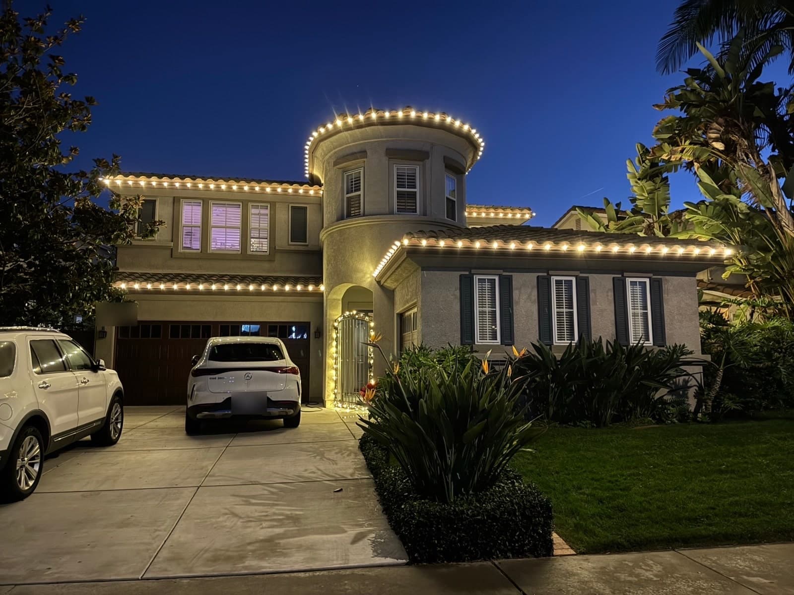 Warm white permanent lighting tracing the eaves and turret of a two-story San Diego home at dusk